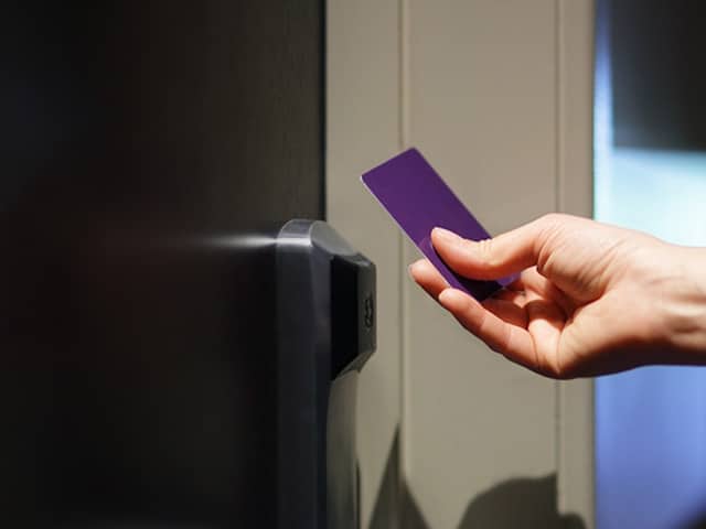 Hand holding an rfid card up to a reader to gain access to a locked door.